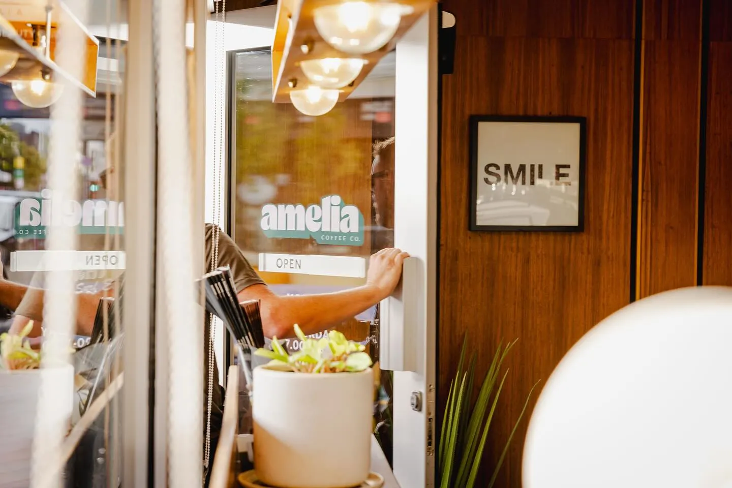 The Amelia Coffee Co. entrance — 'amelia' lettering on glass door with a SMILE print on the warm wooden wall